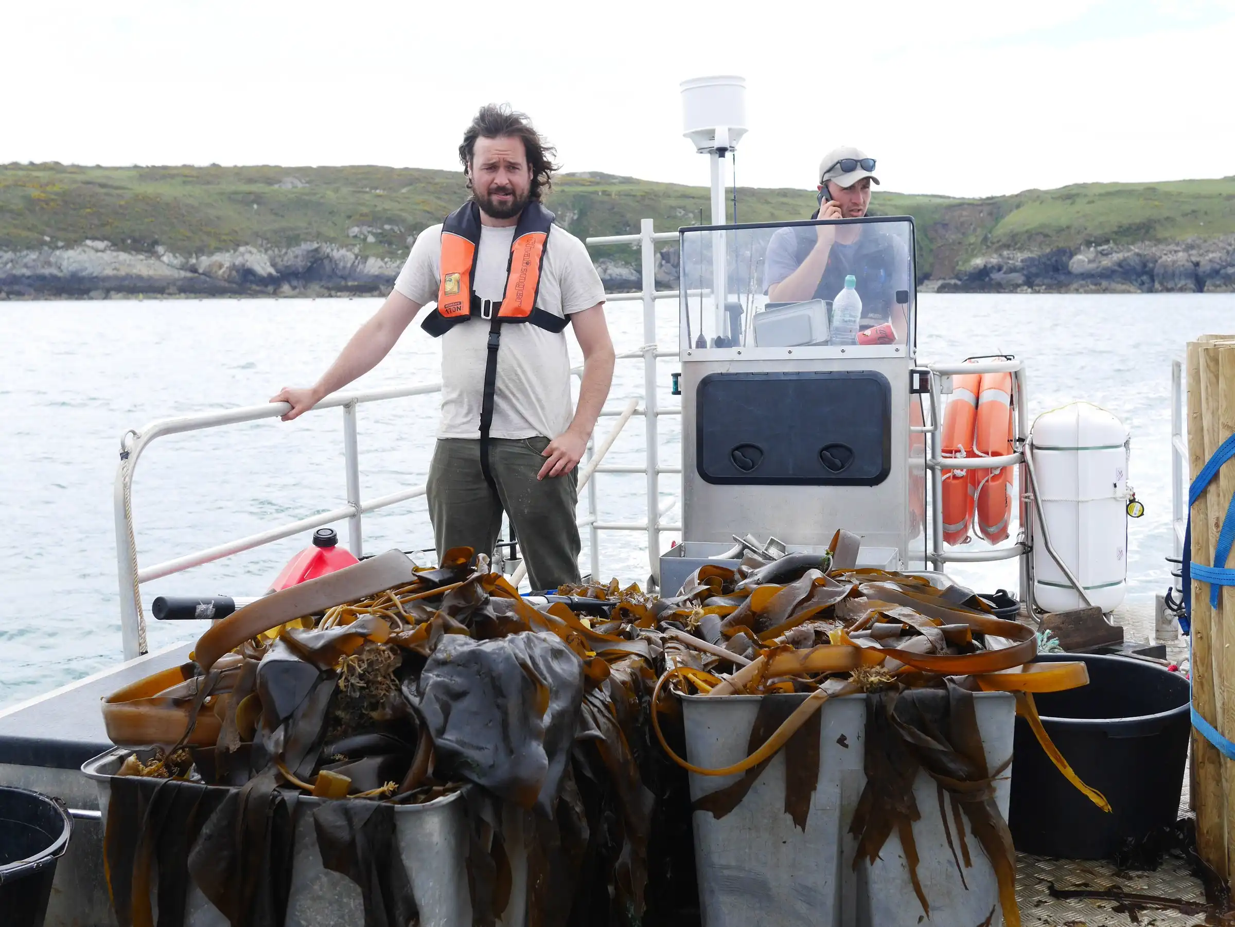 Craig Williams on a boat deck beside harvested seaweed